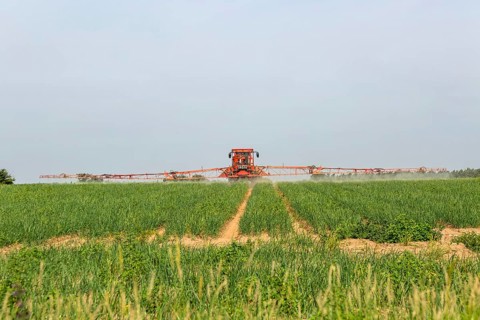 Tractor and crop sprayer spraying arable field, Capel St Andrew, Suffolk, England, UK
