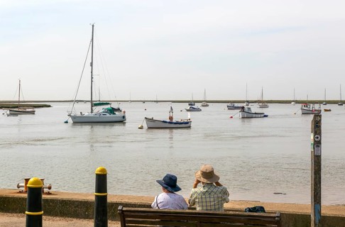People looking out from quayside at boats moored in harbour, River Ore, Orford, Suffolk, England,