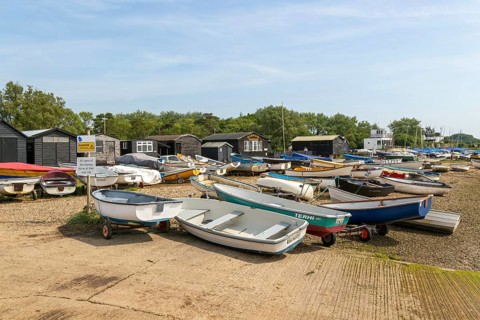 Dinghies on beach with black fishing sheds and Riverside Tearoom cafe, Orford, Suffolk, England, UK