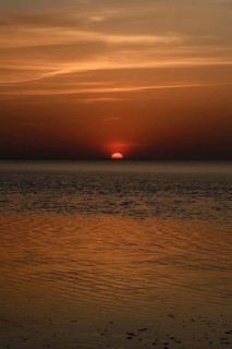 Atmospheric sunset... Cuxhaven, North Sea, in calm weather, glowing red sun sinking into the sea,