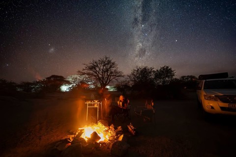 Tourists sitting around a campfire next to their off-road vehicle at night, night shot with starry