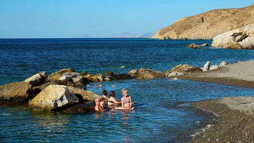 People relaxing in the water on the coast with rocks and clear blue sea, Embros Thermal Baths, Kos,