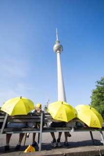 Several people sit with yellow Free Iran umbrellas in front of the television tower on
