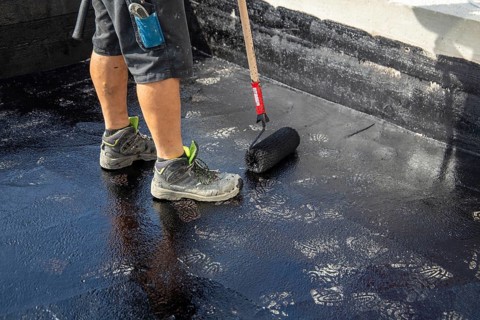 Flat roof waterproofing: Roofer applying the bitumen primer