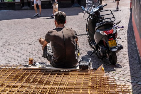 Construction worker taking a lunch break, sitting on wire mats in front of the building site