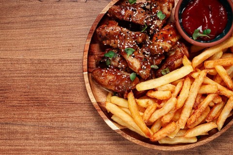Barbecue chicken wings, sprinkled with sesame seeds, with French fries, and sauce, on a wooden