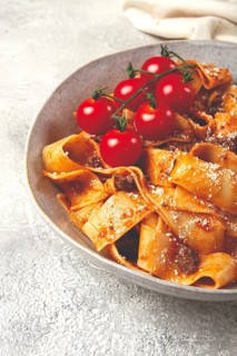 Pappardelle pasta with bolognese sauce, topped with parmesan cheese and cherry branch, homemade, no