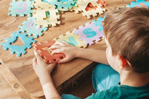 Child assembling colorful puzzle pieces on a wooden table in a bright indoor space during the day