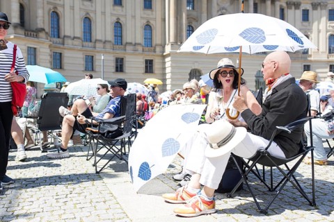 Two visitors under a parasol at the Staatsoper fÃ¼r alle, a free open-air concert with conductor