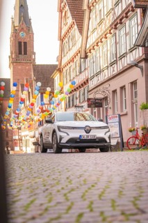 A car on a cobbled street with half-timbered houses and balloons, Deer E, car sharing, electric