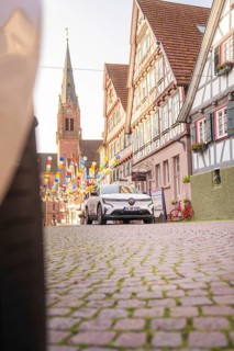 A car drives through a historic town with half-timbered houses and balloons, Deer E, car sharing,