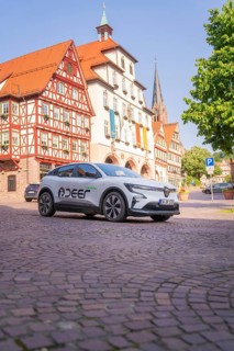 A white car is parked on a cobblestone square next to historic half-timbered buildings with a