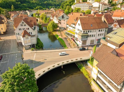 Aerial view of a town with a river and bridge, showing half-timbered buildings and green trees from