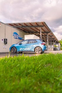 Electric car near an outdoor swimming pool, surrounded by grass and under a cloudy sky, Deer E, car