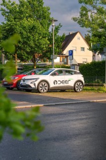 A white electric car parked in a car park in front of a house in a green residential area, Deer E,