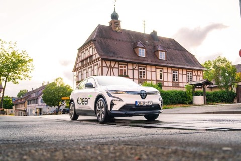 A white electric car drives past a traditional building in a historic town, Deer E, car sharing,