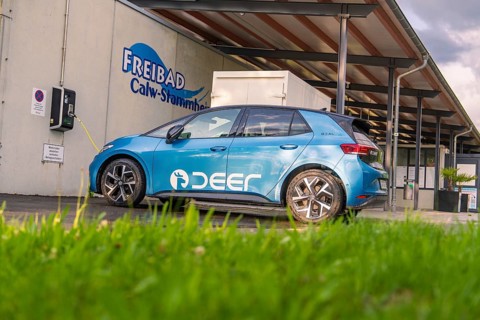 A blue electric car charges at a charging station next to an outdoor pool, Deer E, car sharing,