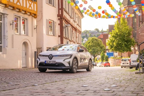 Car drives through a narrow alley, decorated with colourful lanterns, half-timbered architecture