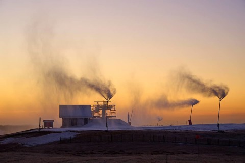 Snow cannons blow clouds of smoke on a hilltop under the purple twilight sky, winter, Route de