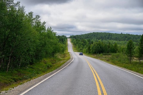 A lonely road leading through a green, wooded hilly landscape of Finland's countryside, Karelia,