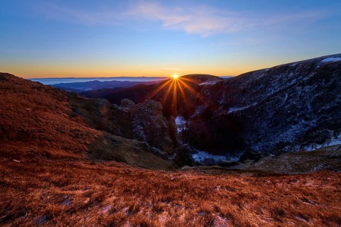 Sunbeams break over the mountains, orange sky and shades of blue, looking towards the Rhine Valley,