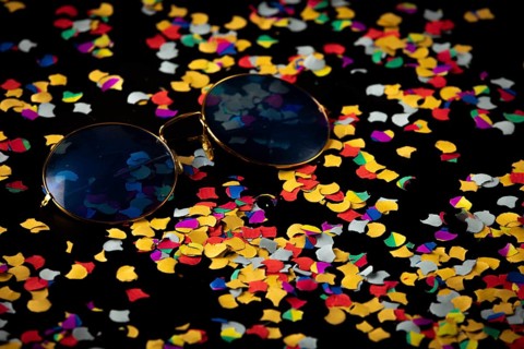 Sunglasses on colorful confetti against black background, Mardi Gras