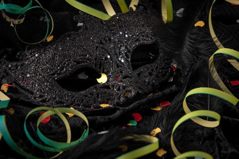 Black carnival mask with colorful confetti and streamers on dark fabric