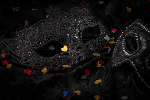 Black mask with confetti on dark background, contrasting carnival atmosphere