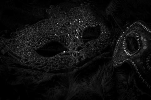 Black masks on a dark background, contrasting carnival atmosphere