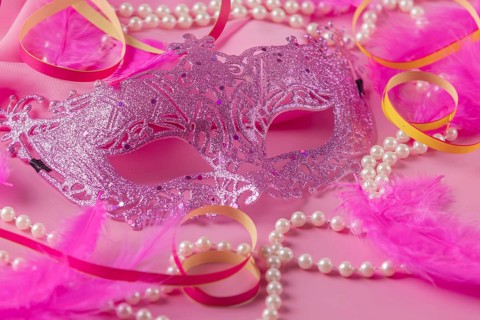 Glittering pink mask with pearls, feathers and colorful streamers on pink background, carnival