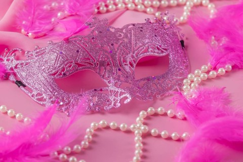 Glittering pink mask on pink background with feathers and pearl necklaces