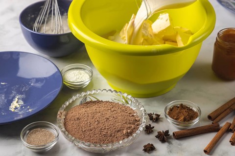 Milk is added to baking ingredients in dough bowls surrounded by cocoa, cinnamon, and other spices
