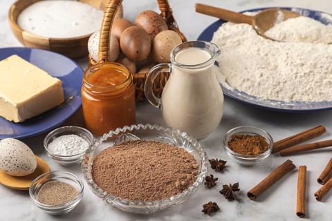 Baking ingredients, flour, sugar, cinnamon, milk, butter, cocoa, jam and eggs on a table