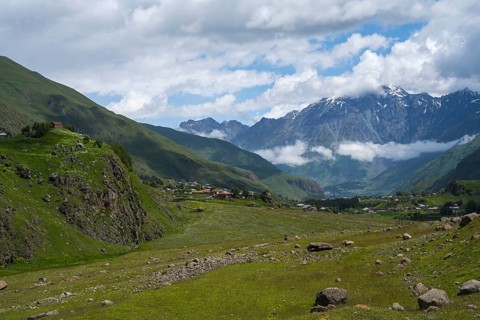 A wide valley stretches against snow-capped mountain peaks under a cloudy sky, Kazbegi, Qasbegi,