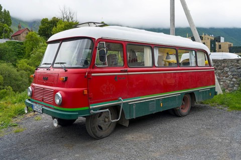 Red retro bus with green stripes on a road in a rural mountain landscape, vintage car, Robor LO