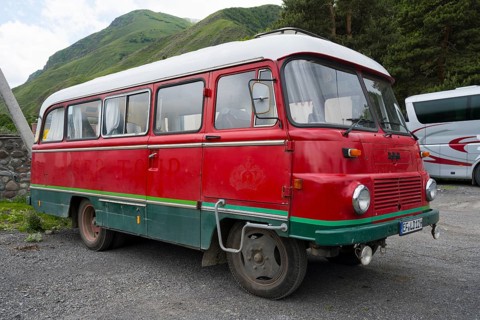 Old nostalgic bus in red with green accent on a parking lot in a mountainous landscape, vintage