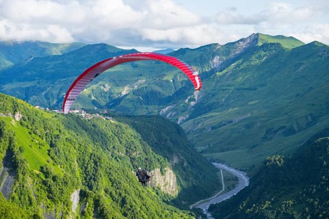 A paraglider floats over a lush green gorge with a winding river, paraglider, paraglider near