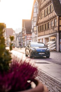 Black car in quiet old town with half-timbered houses and warm sunlight, MG4 electric car, Deer