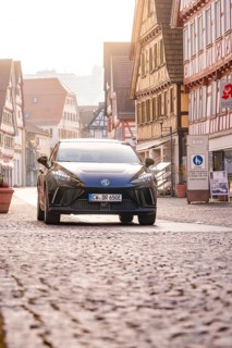 Black car drives through an old town with half-timbered houses and cobblestones, MG4 electric car,