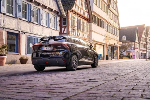 Car standing in front of half-timbered houses in a paved old town street under soft light, MG4