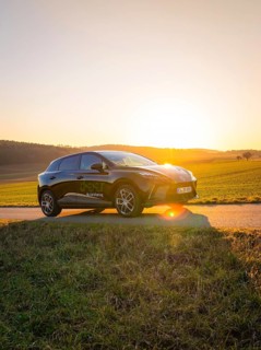 Black car parked on a country road surrounded by green fields when the sun is low, MG4 electric