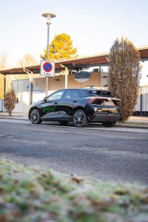 Car parked at the edge of a parking lot with trees and a building in the background, MG4 electric