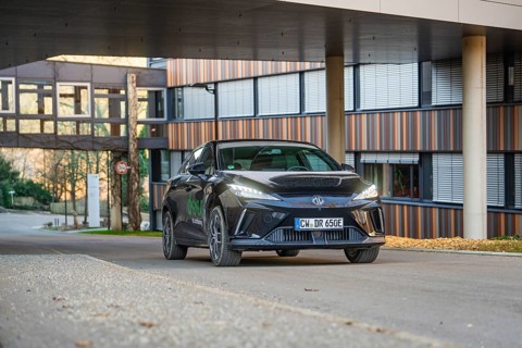 Black car on an urban road in front of a modern building at sunset, MG4 electric car, Deer