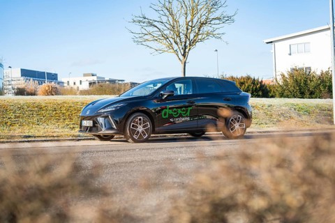 Black car driving along a wintry landscape with modern buildings in the background, MG4 electric