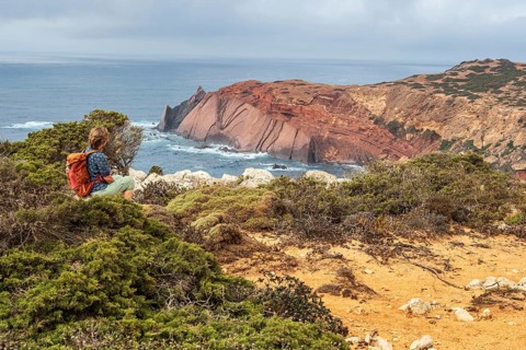 Hiking woman takes a break, view over cliff, Fishermens Trail, Rosa Vicentina, western Algarve just