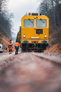 Close-up of a yellow train with workers on rails under cloudy sky, using a tamping machine on the