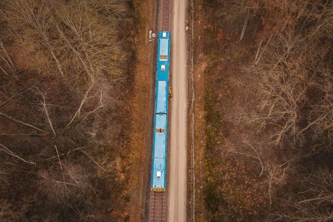 Bird's-eye view of railway line with yellow train in a wooded region, using a tamping machine at