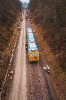 Yellow train on a construction site in a wintry landscape, surrounded by trees, using a tamping