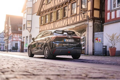 Black car from behind in a street with historic half-timbered houses in daylight, MG4 electric car,