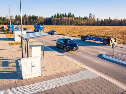 A car turns onto a wide road surrounded by parked vehicles and fields, MG4 electric car, Deer E-
